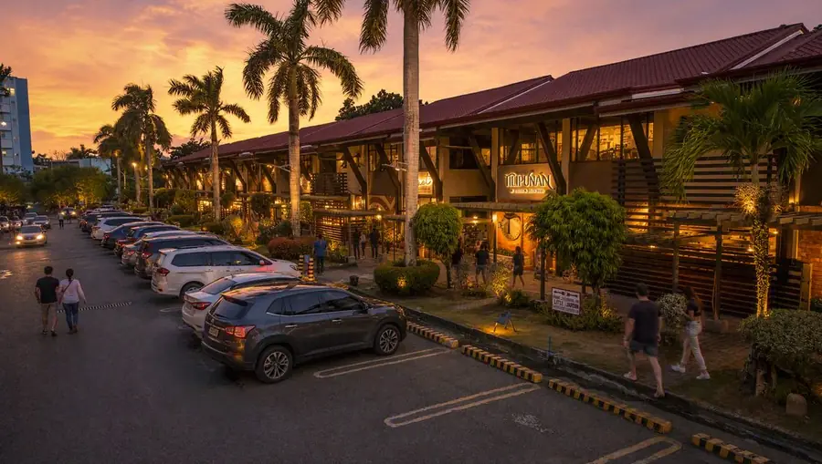 The Boardwalk at sunset, lit storefronts and Tilipunan's sign, people walking along the row